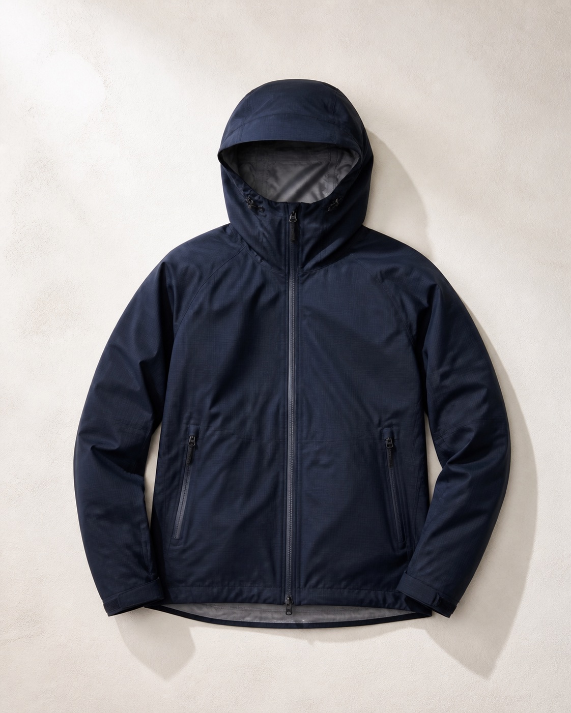 Unbranded navy technical shell jacket photographed flat on a warm neutral surface