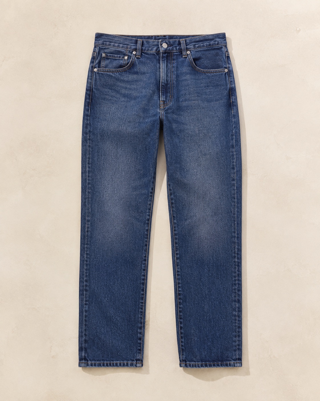 Unbranded straight-leg indigo jeans photographed flat on a warm neutral surface